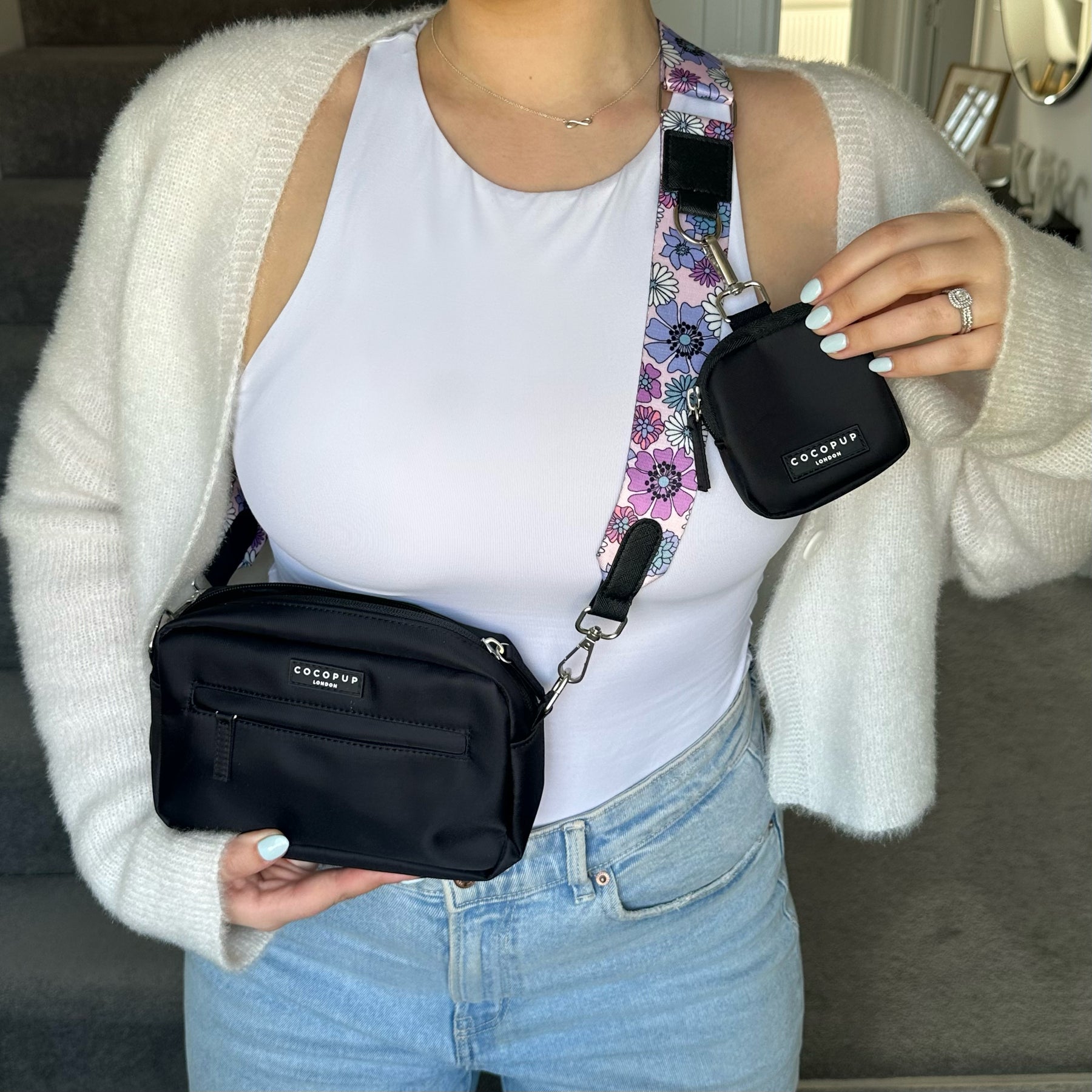 Person wearing a crossbody bag and holding a small pouch with floral strap.