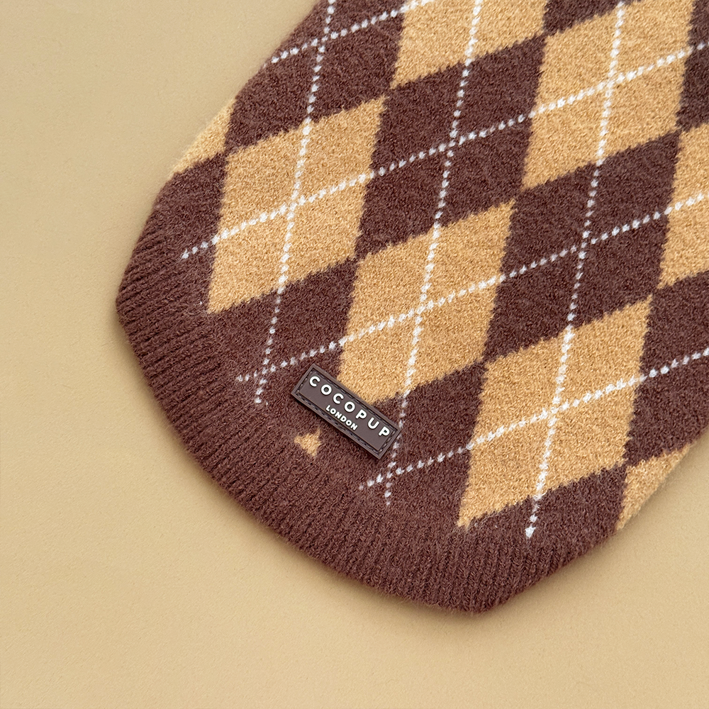 Close up of the bottom of a dog jumper in a brown, tan, and white argyle pattern. 