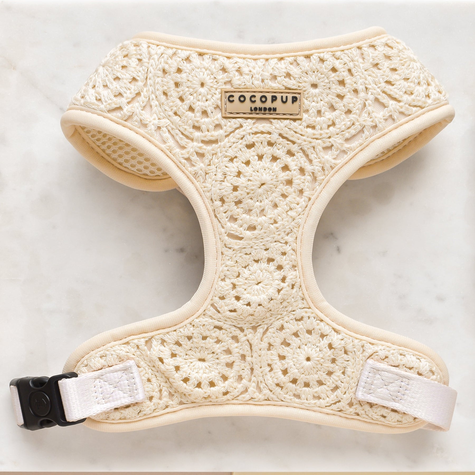 Crochet-patterned dog harness with a 'COCOPUP London' label on a marble background.