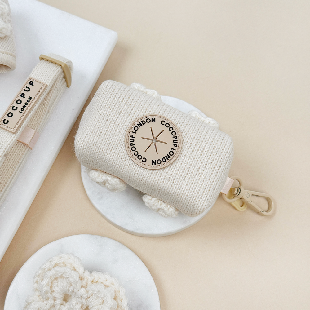 Beige knitted pouch with beige metal clip and hole to put poop bags through.