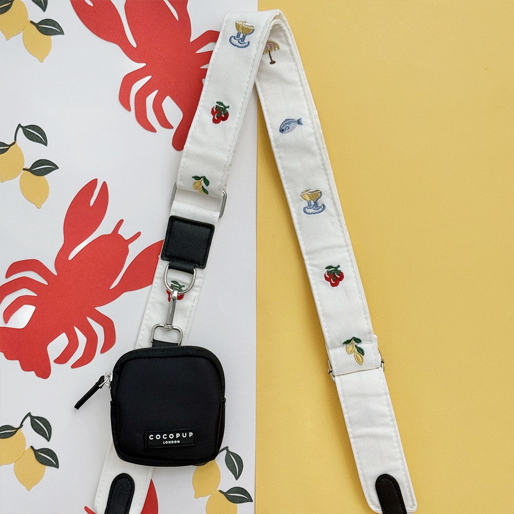 White linen fabric Bag Strap with summer embroidered embellishments. Attached to a black Cocopup Treat Pouch.