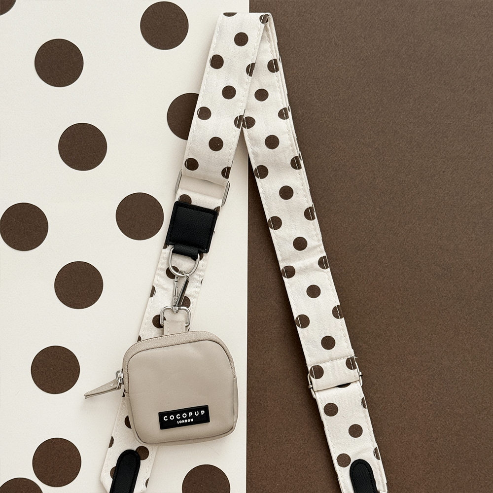 Small beige bag with a polka dot strap on a brown and white polka dot background