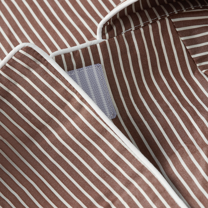 Close-up of a brown and white vertically striped fabric garment, showing the collar area with white piping and a small light blue-gray woven label.