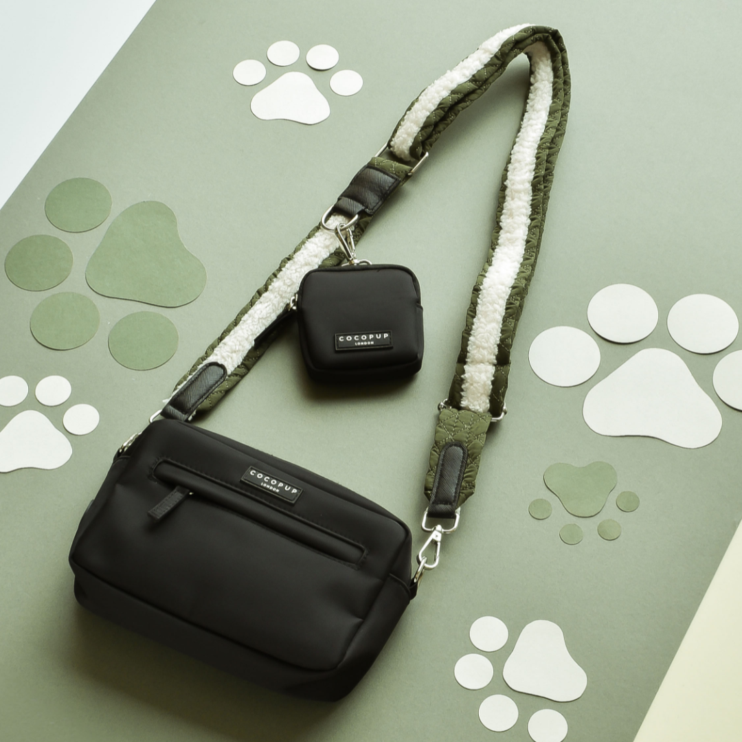 A Cocopup London Dog Walking Bag with khaki quilted straps and a matching small pouch is laid on a green background decorated with white paw prints. The bag and pouch feature brand labels reading "Cocopup London.