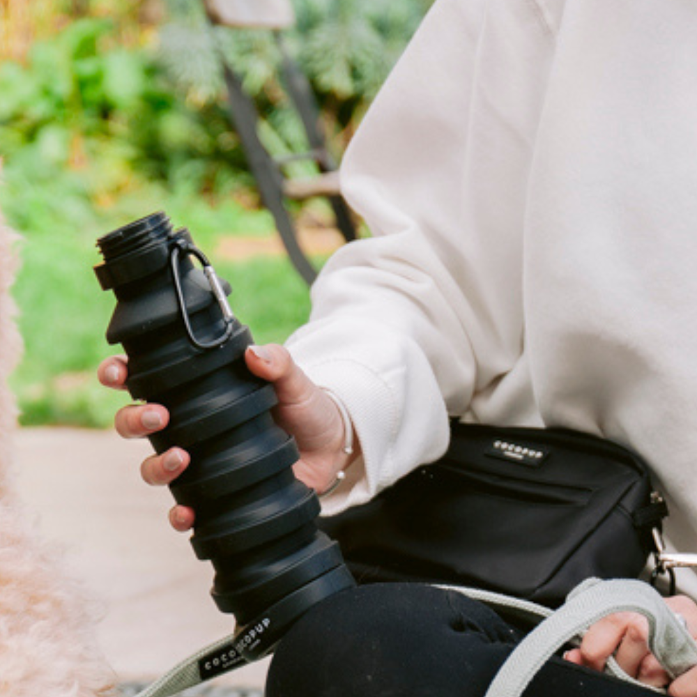 Model holding the the Cocopup Black Water Bottle Cup whilst wearing the Cocopup Black Dog Walking Bag.