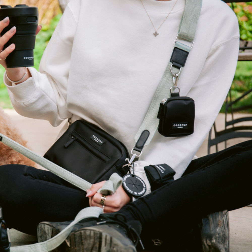 Person holding a coffee cup, wearing a white sweatshirt and a black crossbody bag.