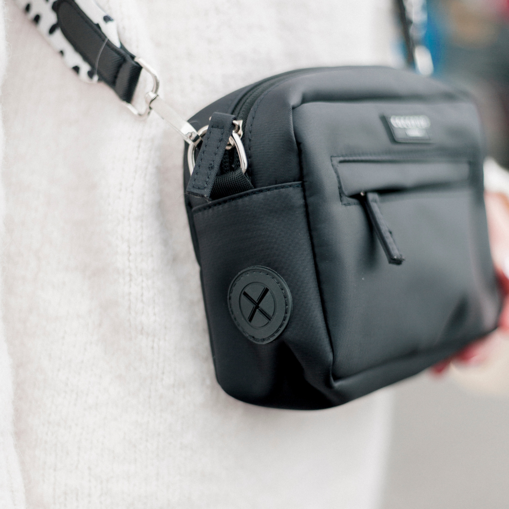 Close-up of a black crossbody bag with a zipper and a patterned strap.